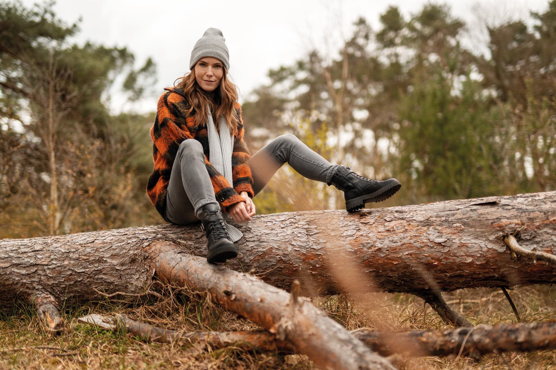 Frau mit schwarzen Schnürboots sitzt im Wald auf einem Baum