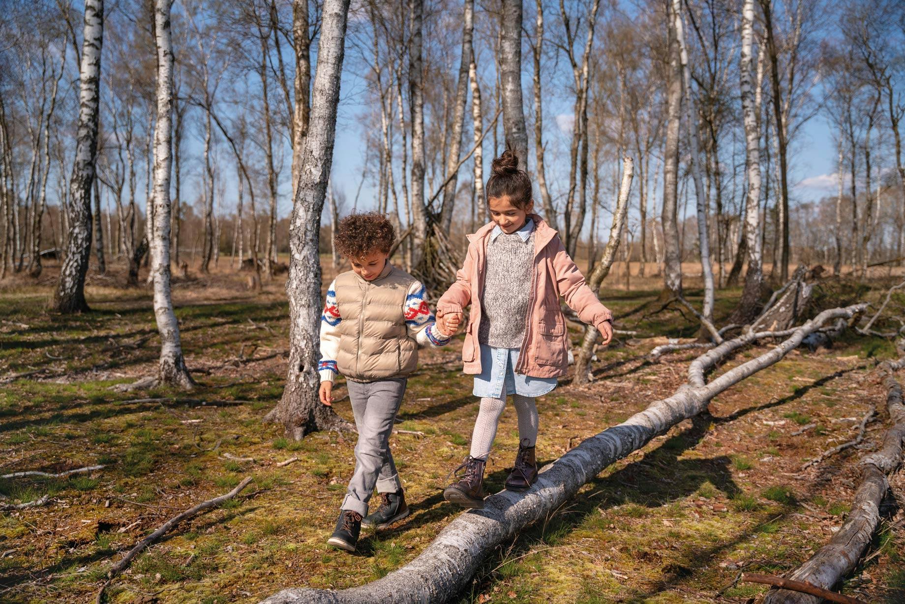 Zwei Kinder spielen mit neuen Schuhen im Wald auf Bäumen